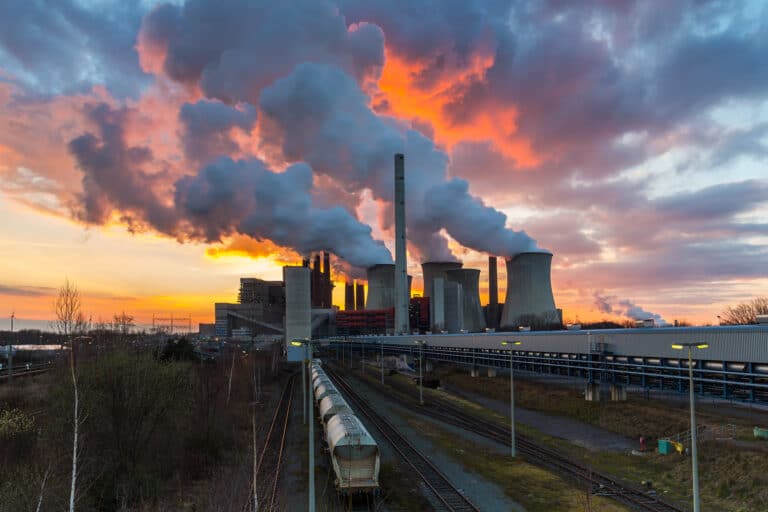 Power station at sunset with smoke billowing out of the chimneys across the sky.
